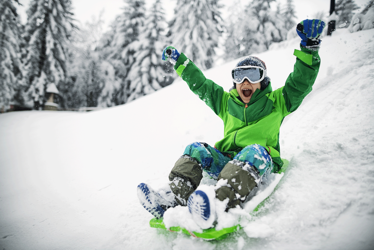 Little boy having extreme winter fun on sled. The boy is sledding down hill and yelling.